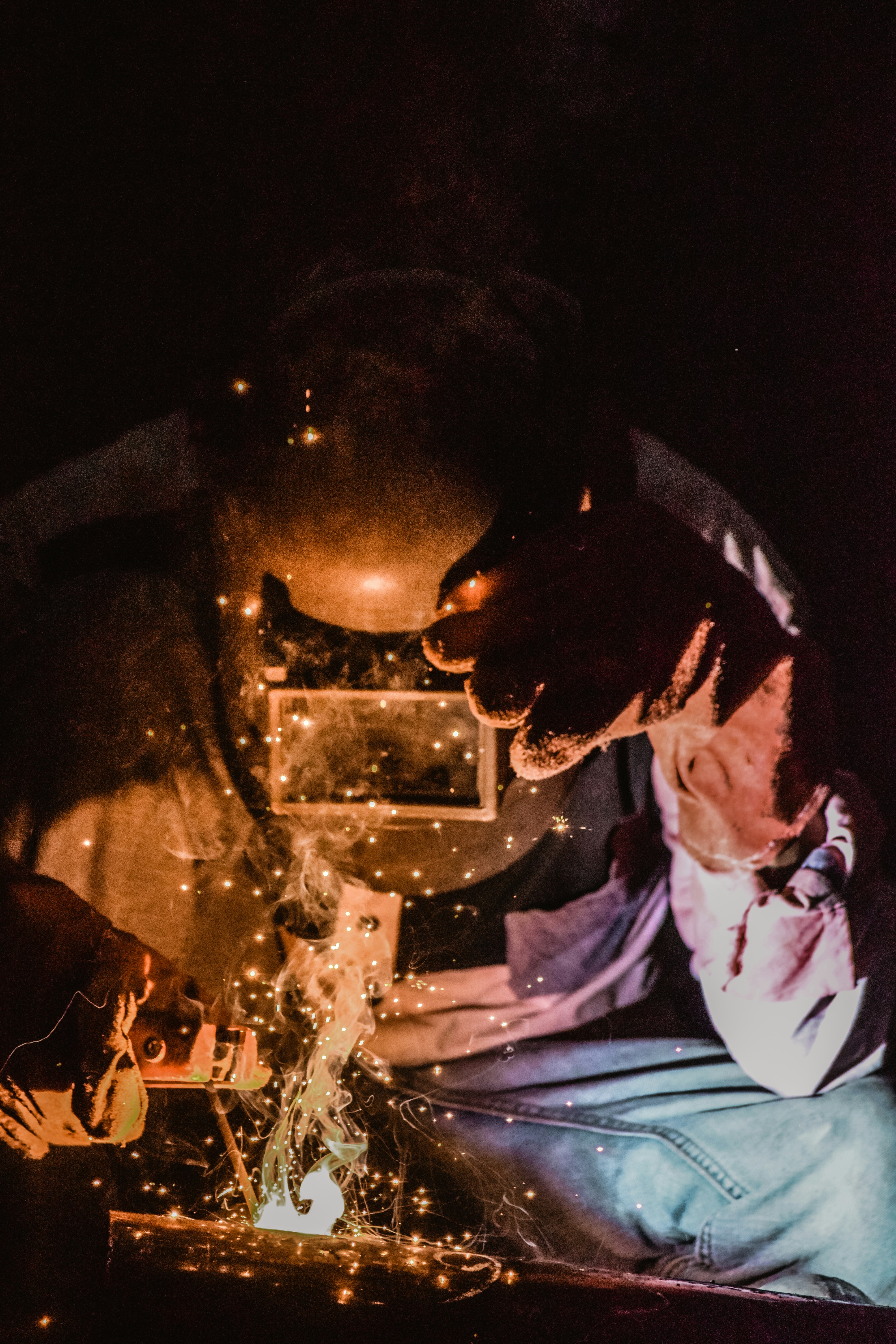 Welder working on a metal joint with orange sparks